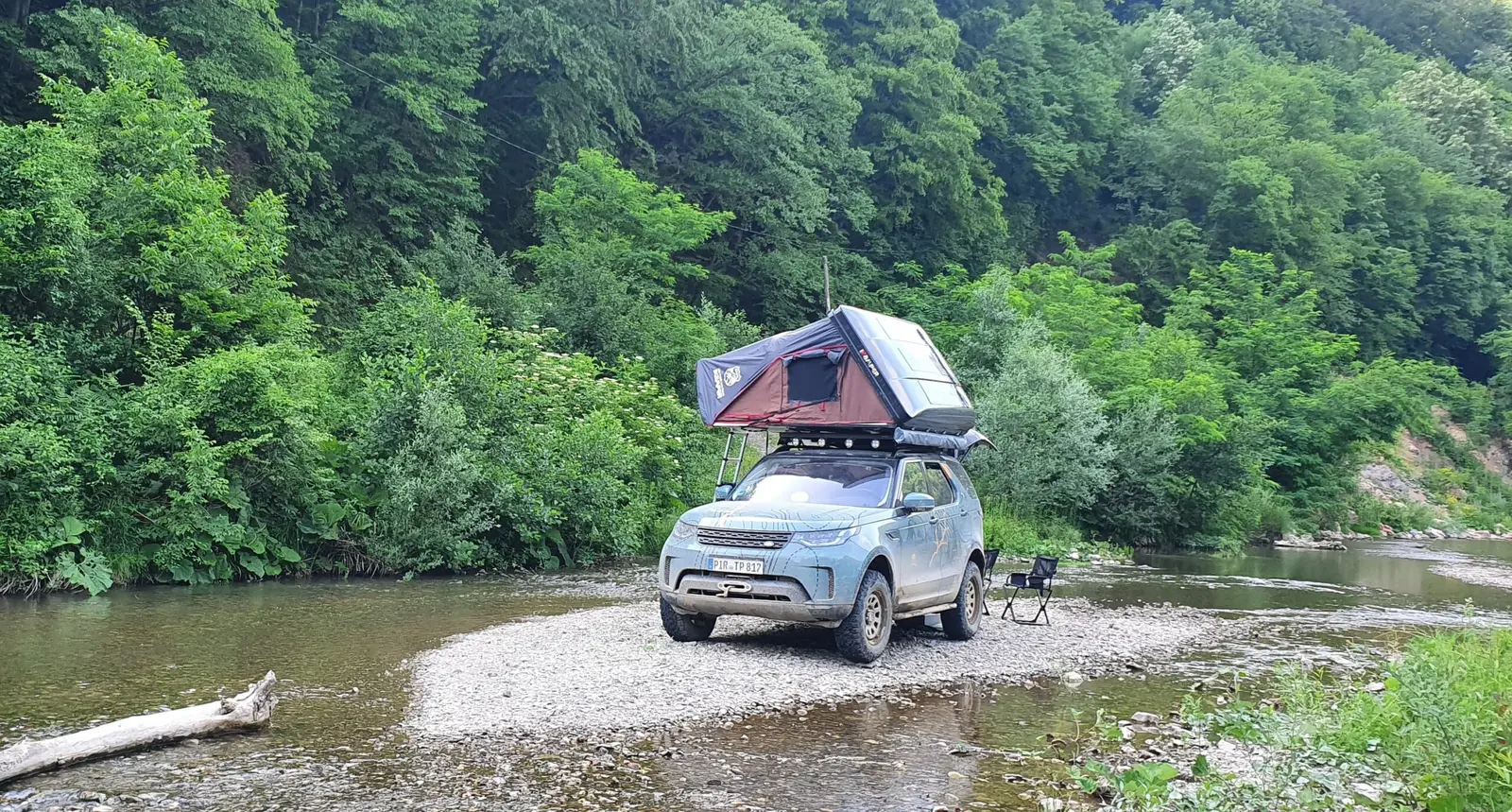 Land Rover Discovery with rooftop tent parked on a river bank
