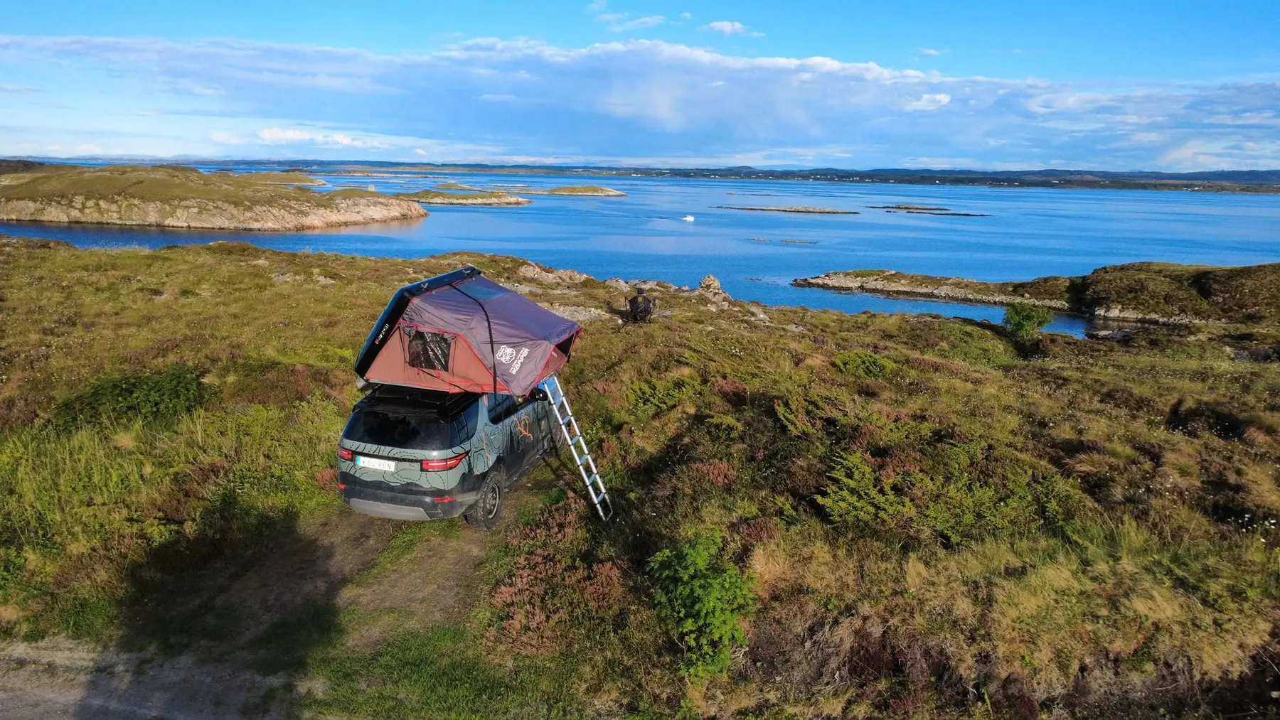 Land Rover Discovery with open rooftop tent above the Norwegian coast