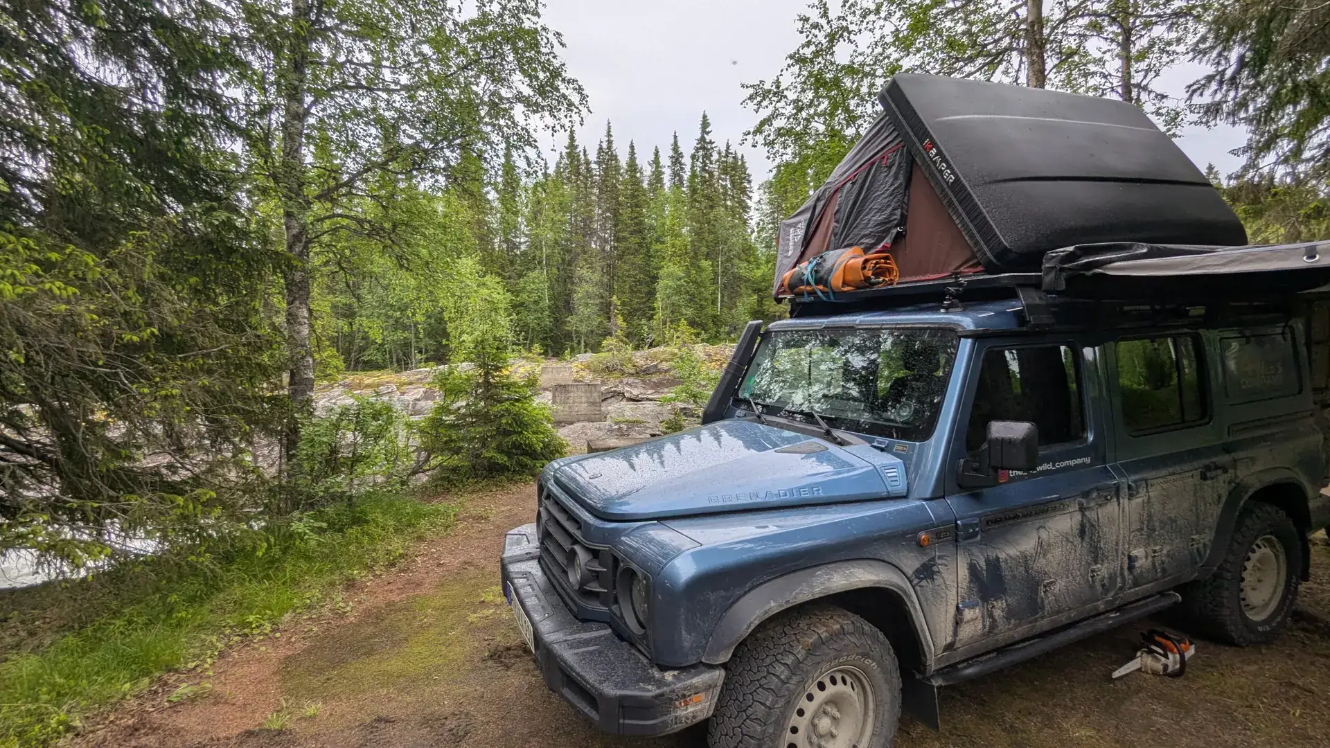 Ineos Grenadier with open rooftop tent and awning at a forest camp