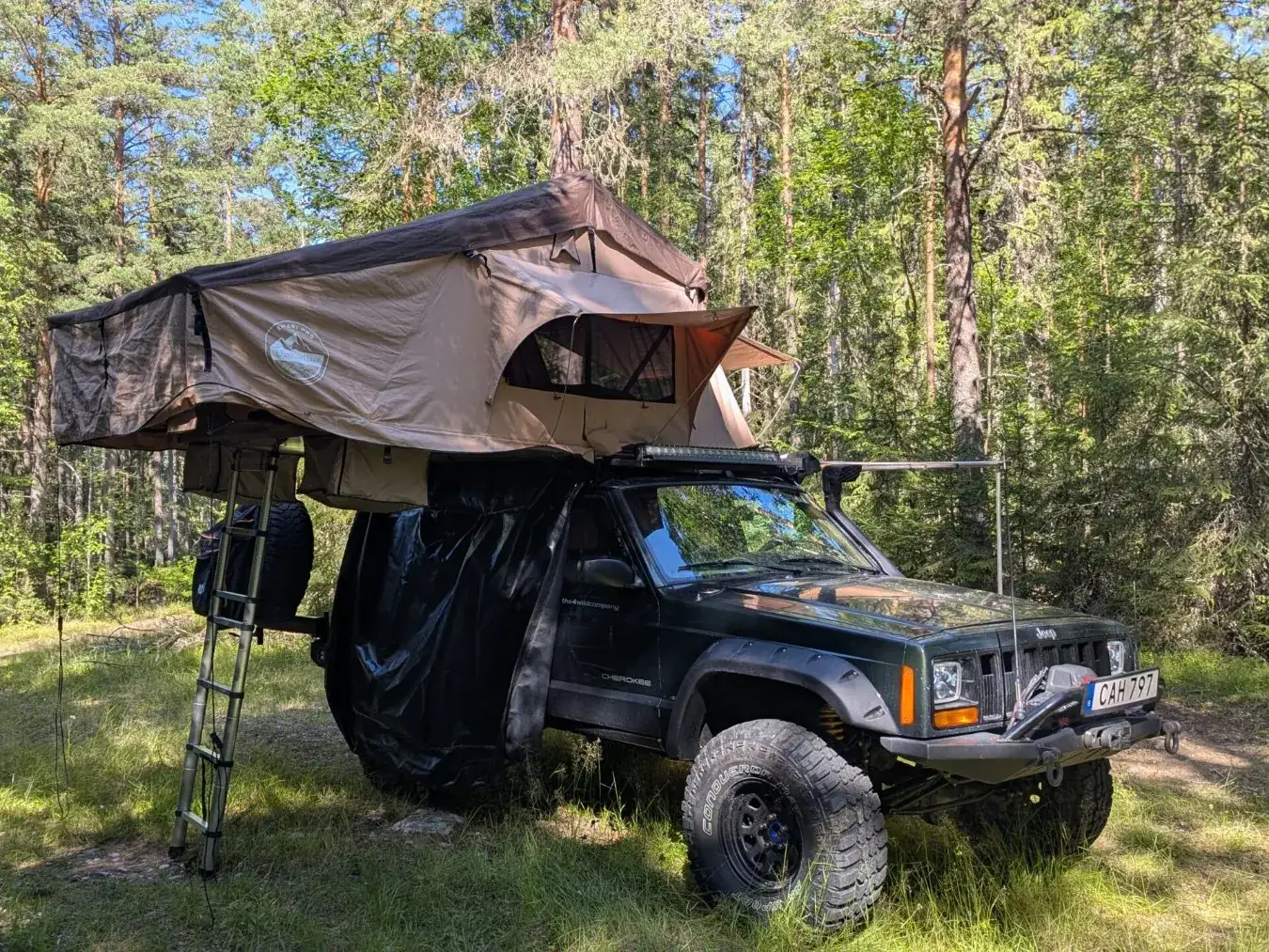 Jeep Cherokee XJ with open rooftop tent in the forest