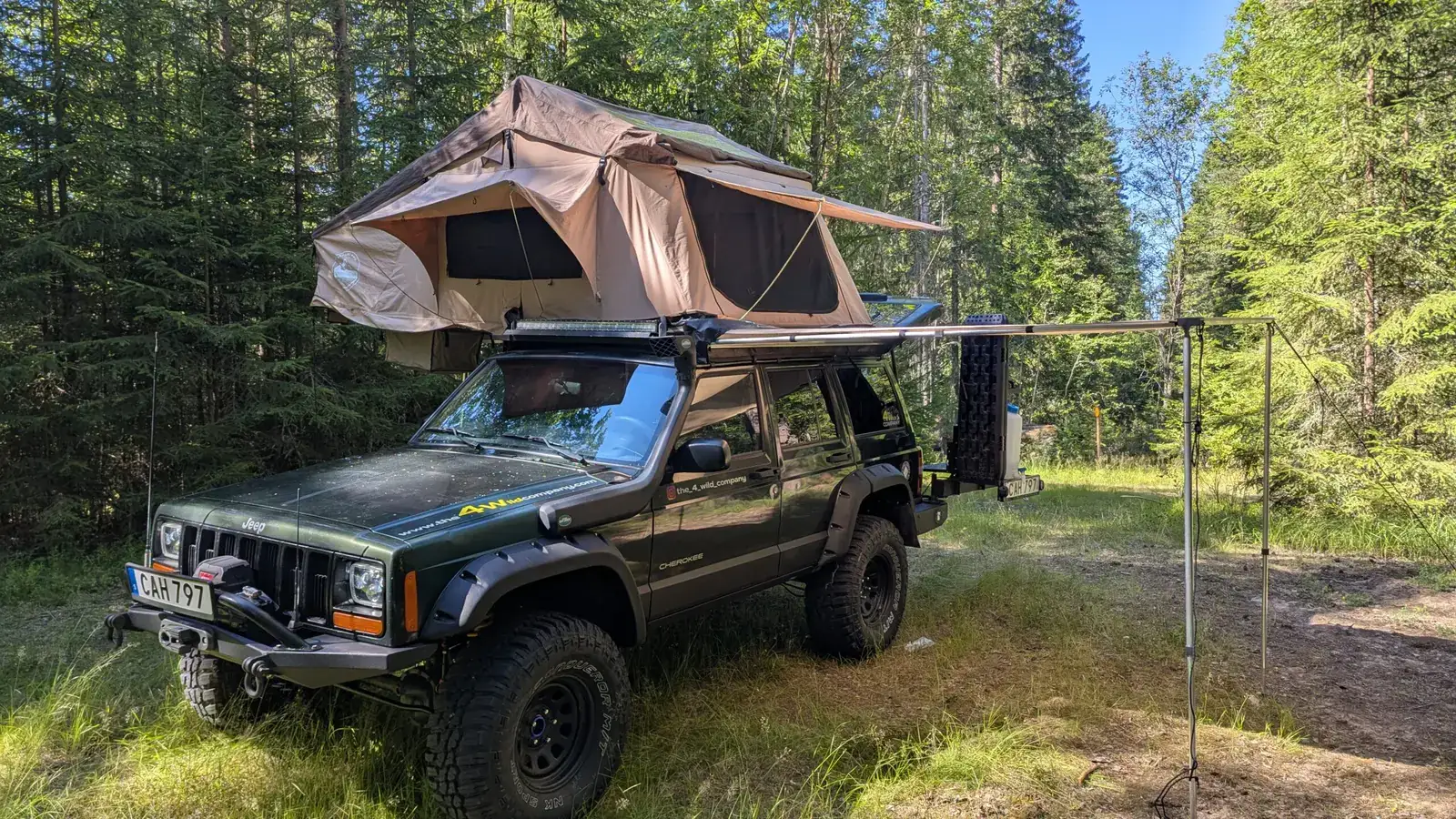 Jeep Cherokee XJ with open rooftop tent in a pine forest