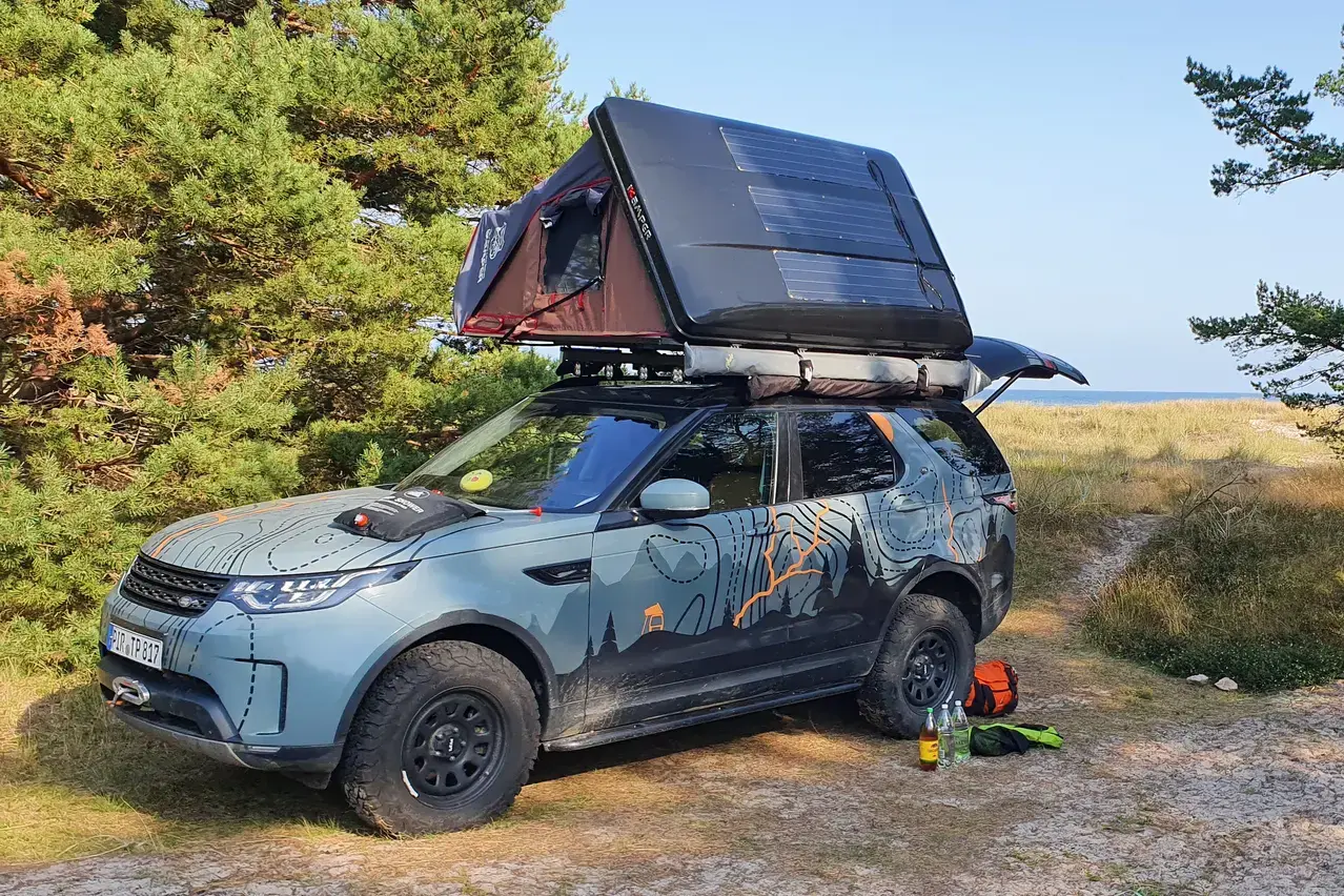 Land Rover Discovery with rooftop tent among pine trees