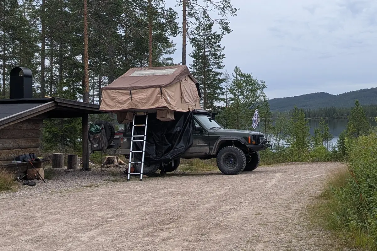 Jeep Cherokee XJ with open rooftop tent by a lake