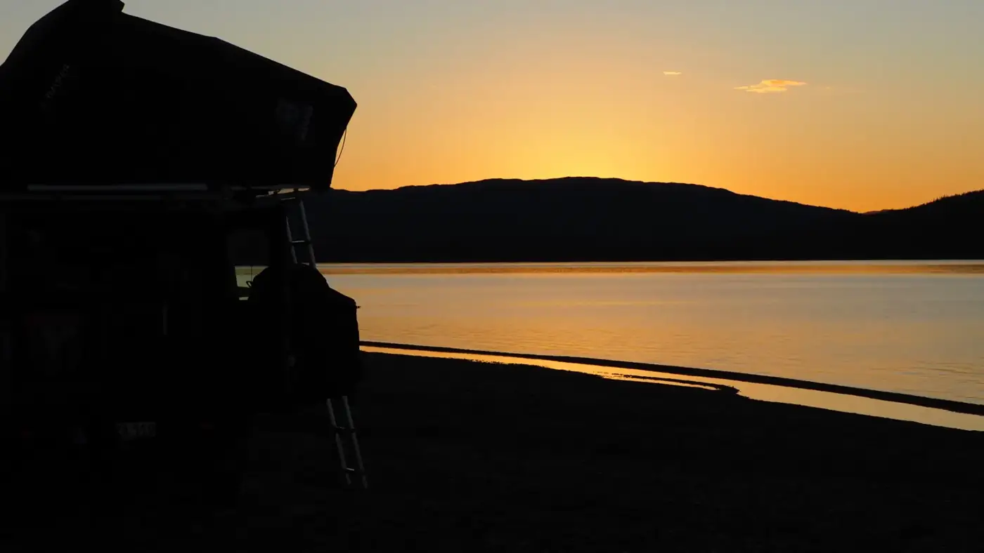 Rooftop tent by a lake at sunset