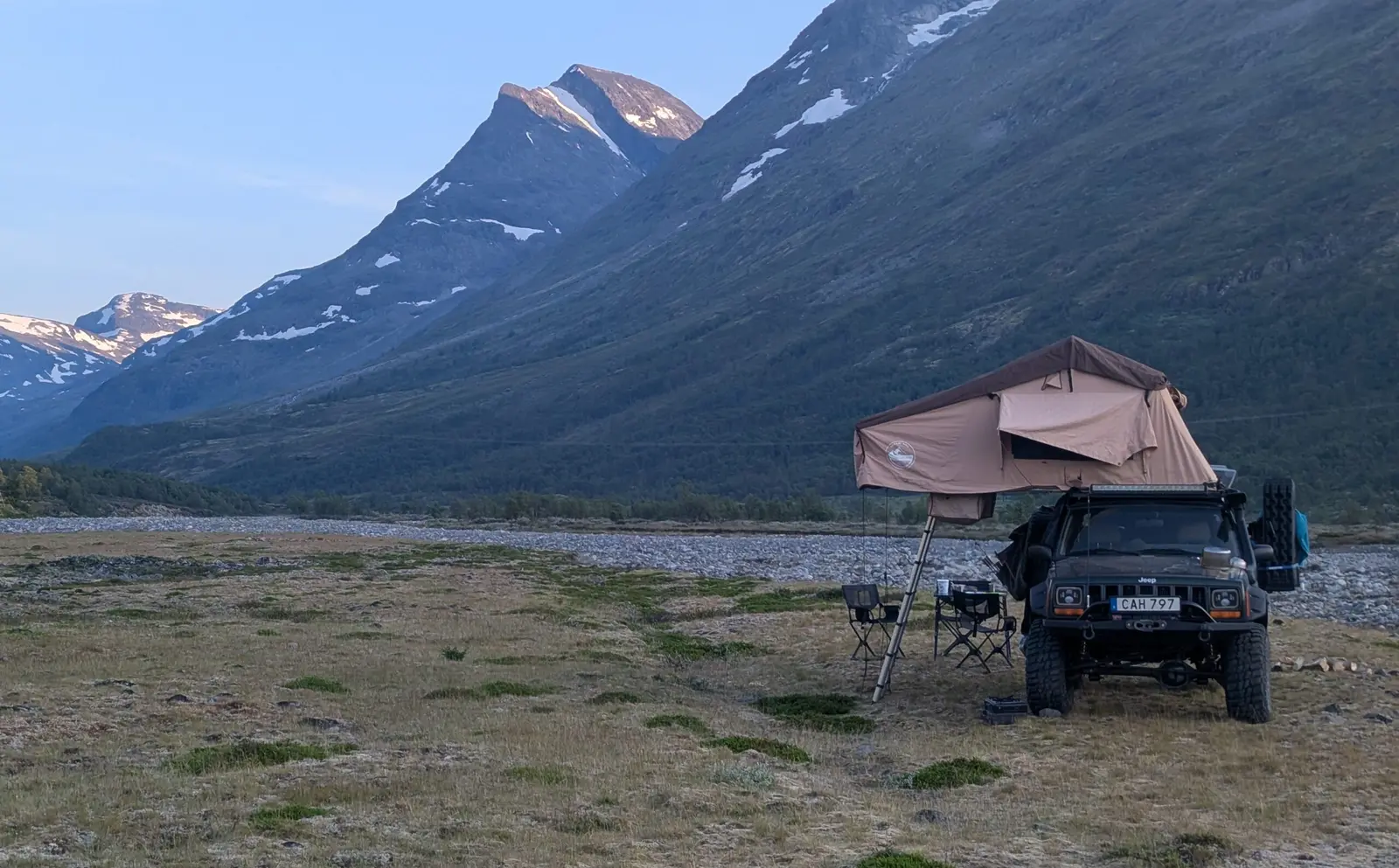 Jeep with open rooftop tent below snowy mountains