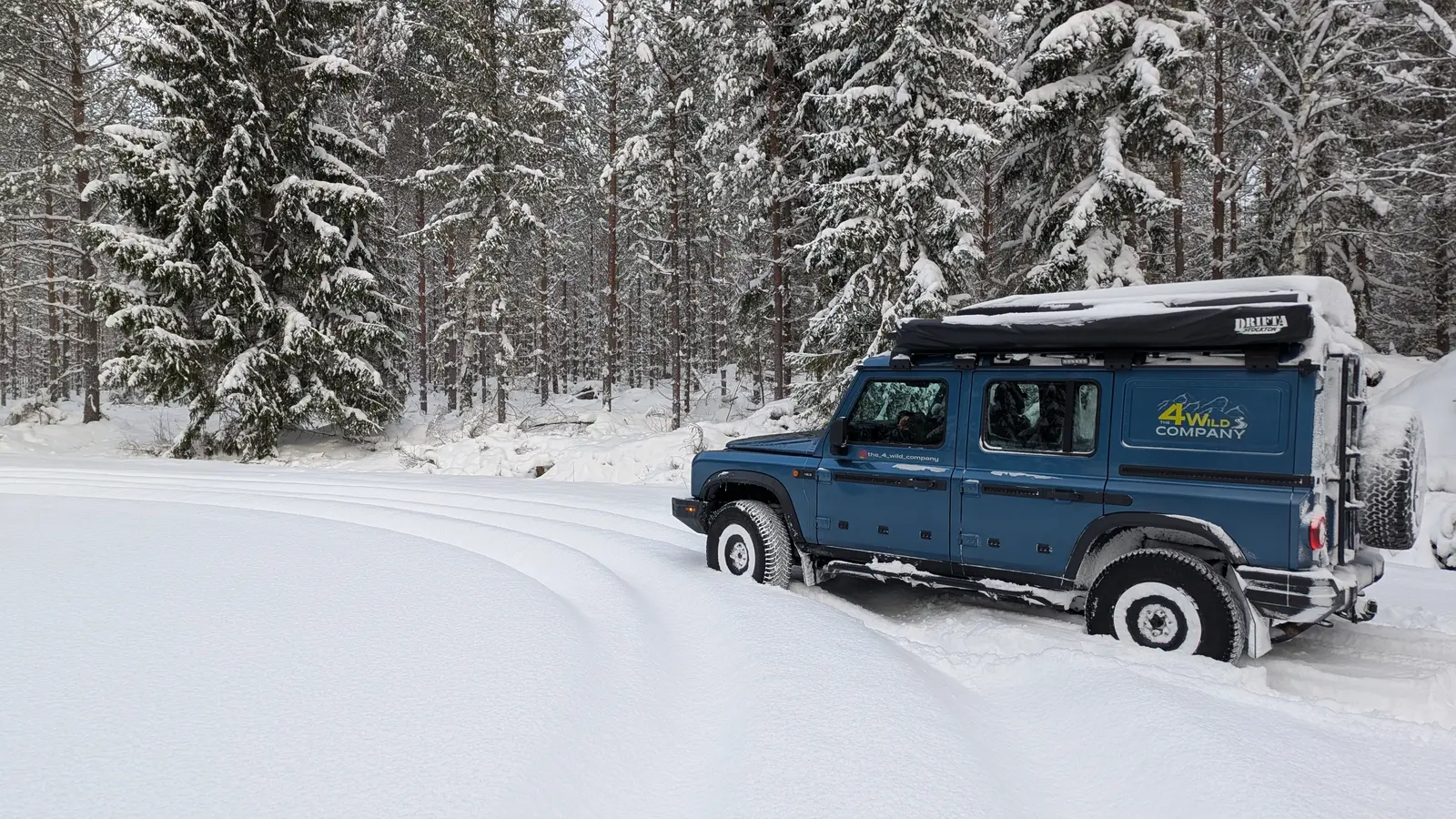 Ineos Grenadier with rooftop tent in deep snow between pine trees